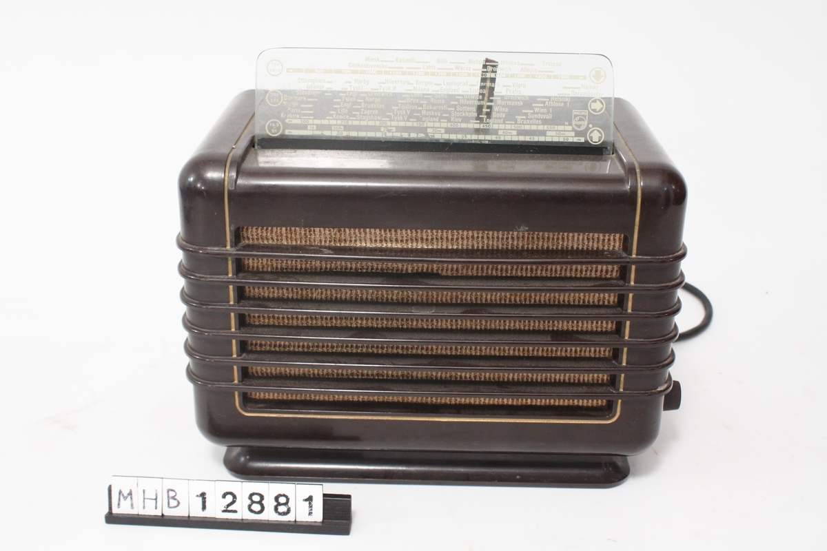 Radio av type Philips 209 U - 32. Radioen er kompakt. Rett firkantet prismeform. Høytaleren i lysebrunt tøy skimtes igjennom metallriller i  radiokassen. På toppen skrå glassplate, hvor stasjonerr kan avleses. Ledningen med stikkontakt er festet i radiones bakside. Knapper på hver side for av/på, volum og stasjoner.