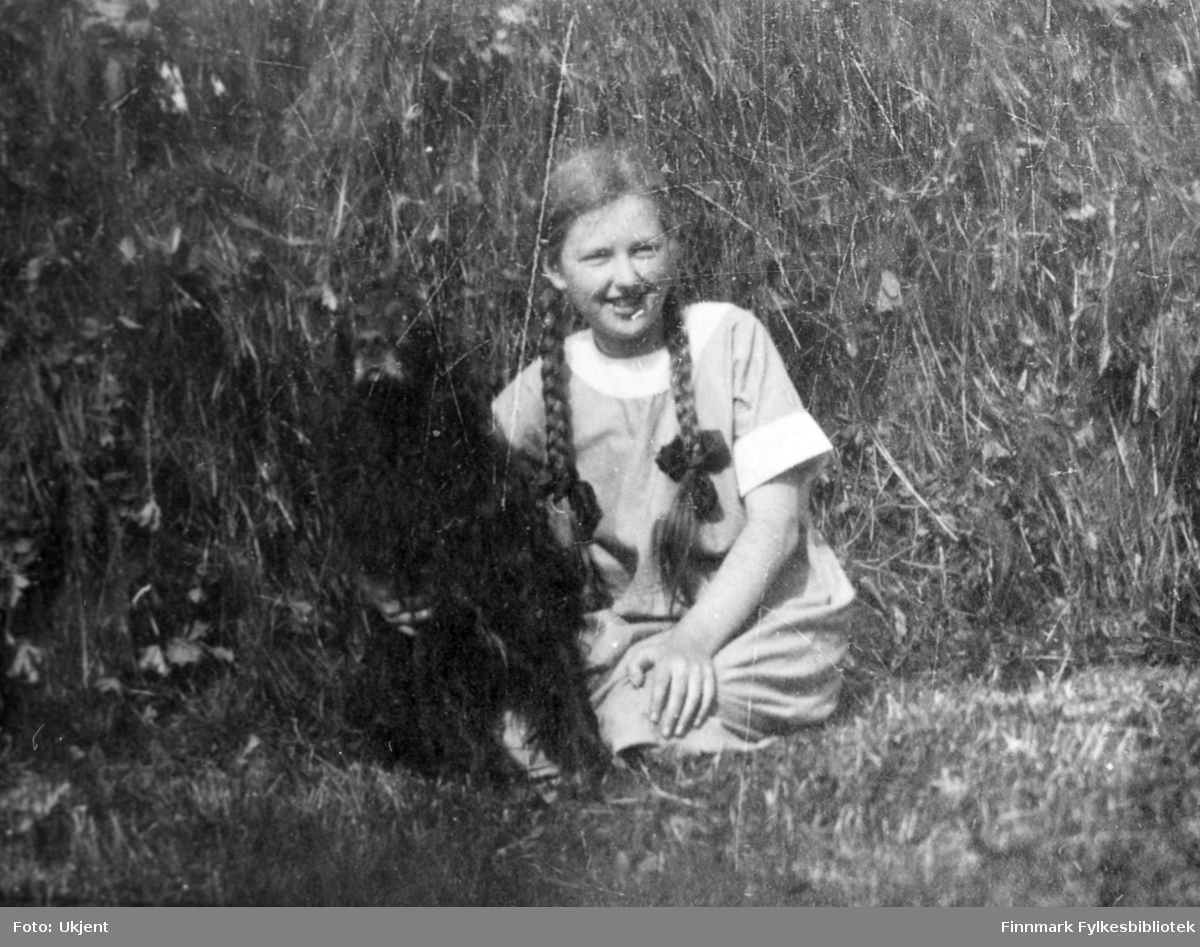 Bildet trolig tatt Sommeren 1923 i Jarfjord. Piken på bildet er Aagot Bertelsen, ved siden av henne sitter en mørk hund som trolig er familiehunden 'Tussemann'. Aagot har på seg en kjole og har flettet hår med sløyfer. Hun sitter på bakken og holder rundt hunden.