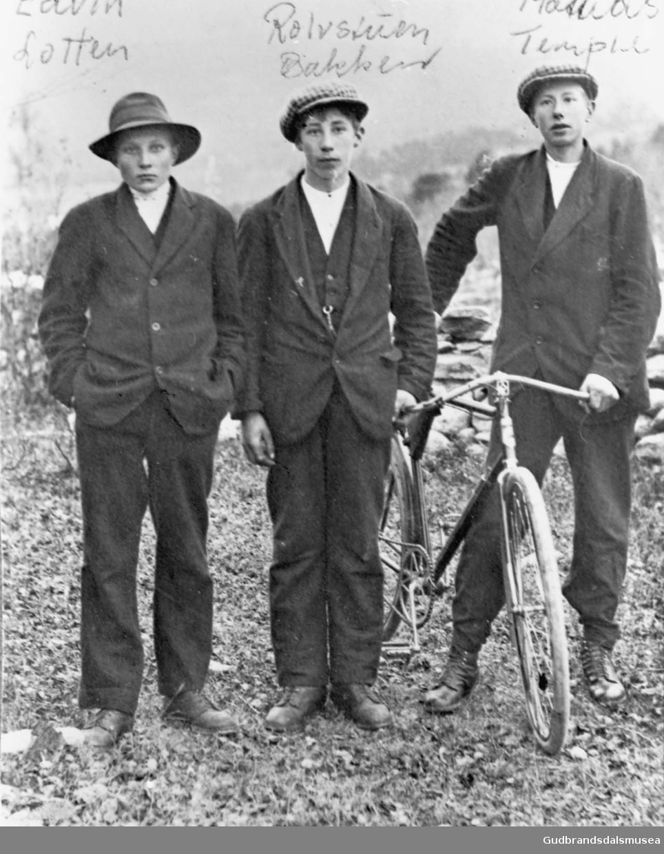 Tre eldre gutter med sykkel, landskap i bakgrunnen. 

