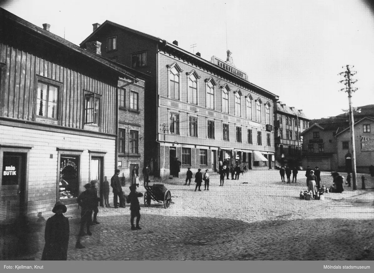 Det stenlagda gamla torget med kärror, folk och kommunalhuset som fasad. J.A. Jonssons brödbutik i förgrunden. Antagligen innan år 1919.