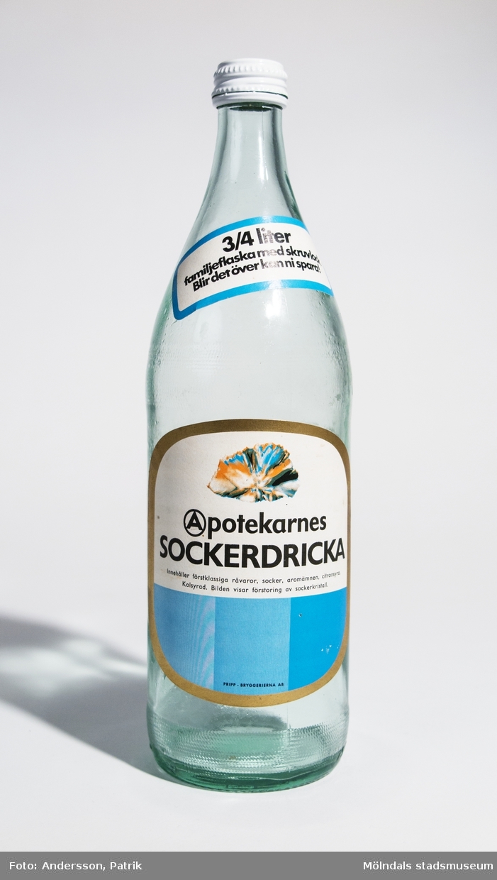 Glasflaska med vit och blå etikett från Apotekarnes, tidigare inhåll 3/4 liter sockerdricka.