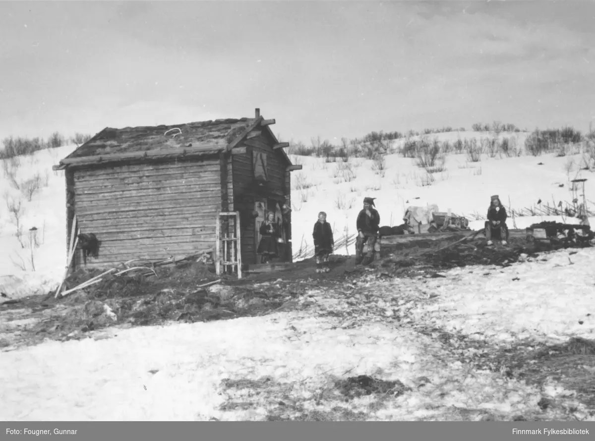 Fire samer, en mann og tre barn, utenfor boligen sin, en hytte av laftet tømmer.
