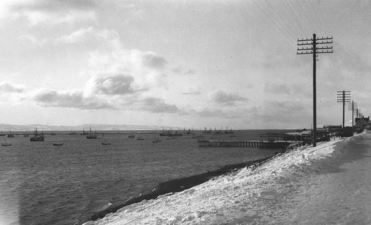 Vinterbilde fra Vadsø havn før andre verdenskrig, tatt fra Havnegata. Mange småbåter ligger fortøyd, noen større fartøy ses lengre ut i havna.
