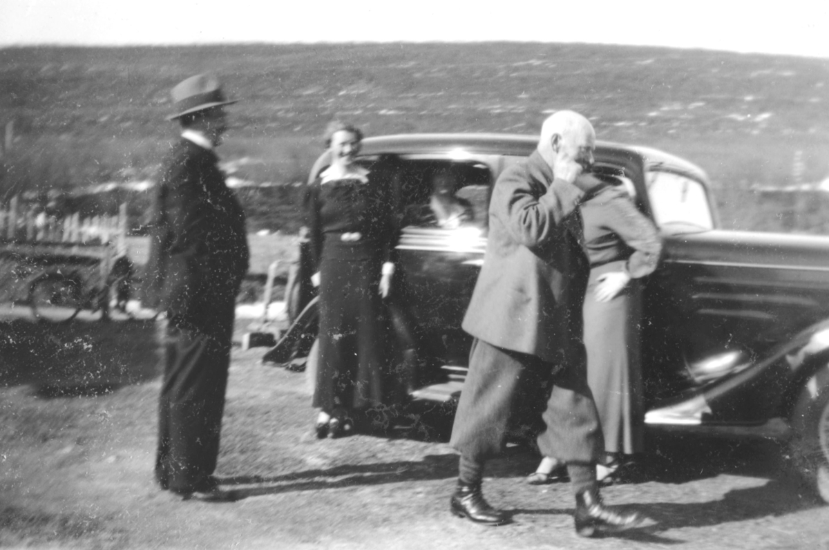 Damer og menn som står ved siden av en bil, en Chevrolet 1934 modell.