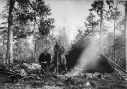 En ung kvinne og en eldre mann utenfor en lavvo, omgitt av f