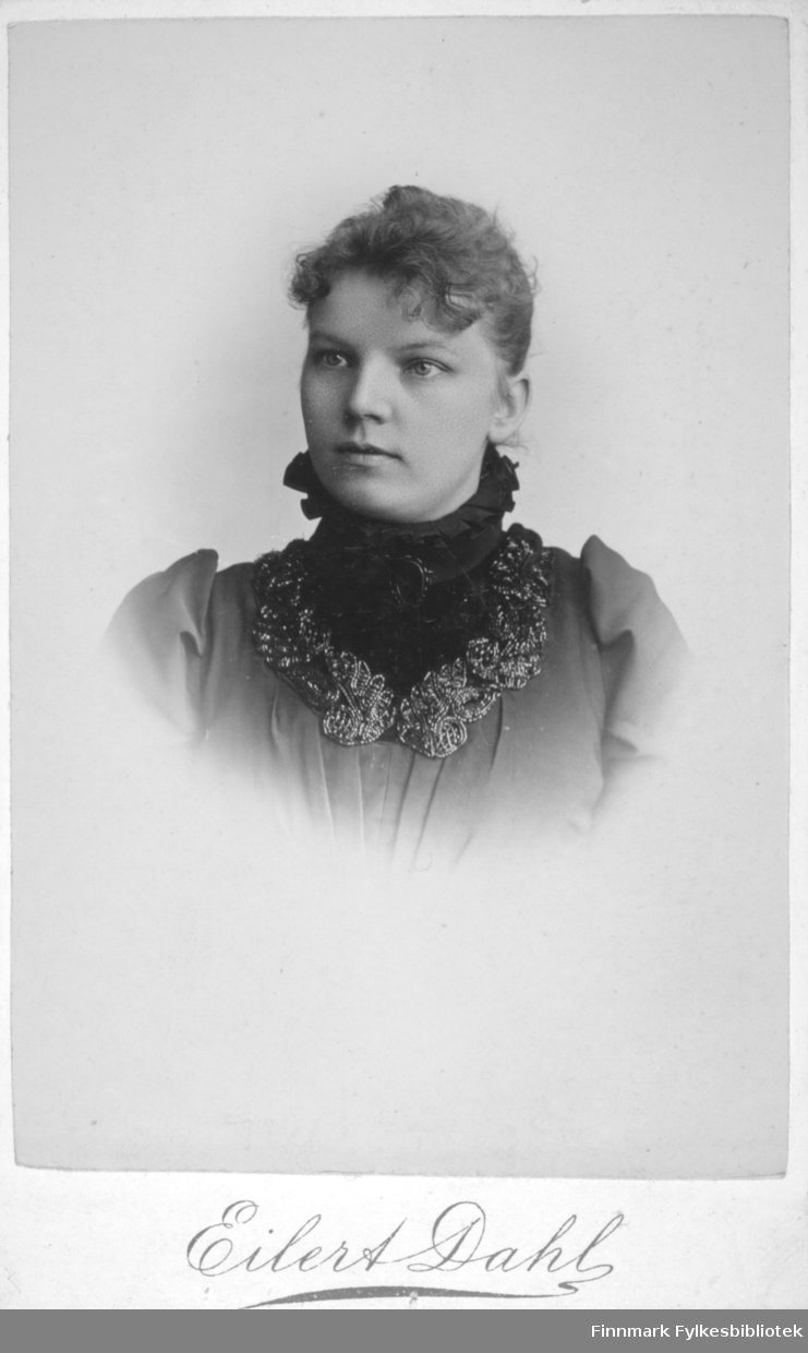 Portrett av en kvinne i mørk bluse med rysjer. Hun har en mørkere løskrage med høy hals. Portrettet er tatt hos Eilert Dahl i Molde.