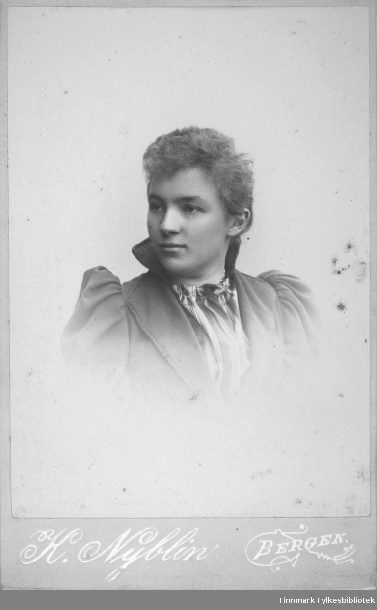 Portrett av en kvinne iført en mørk overdel med skulderputer og en litt lysere bluse under.