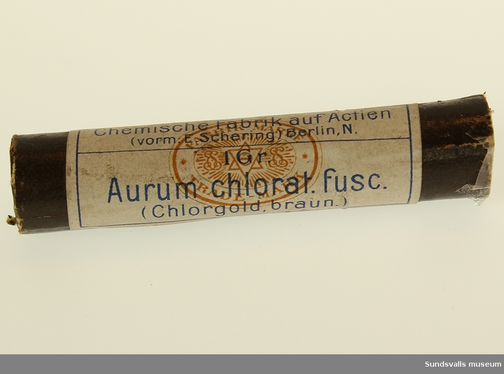 Brun tudelad pappersbehållare med vit tryckt etikett innehållande auric klorid.