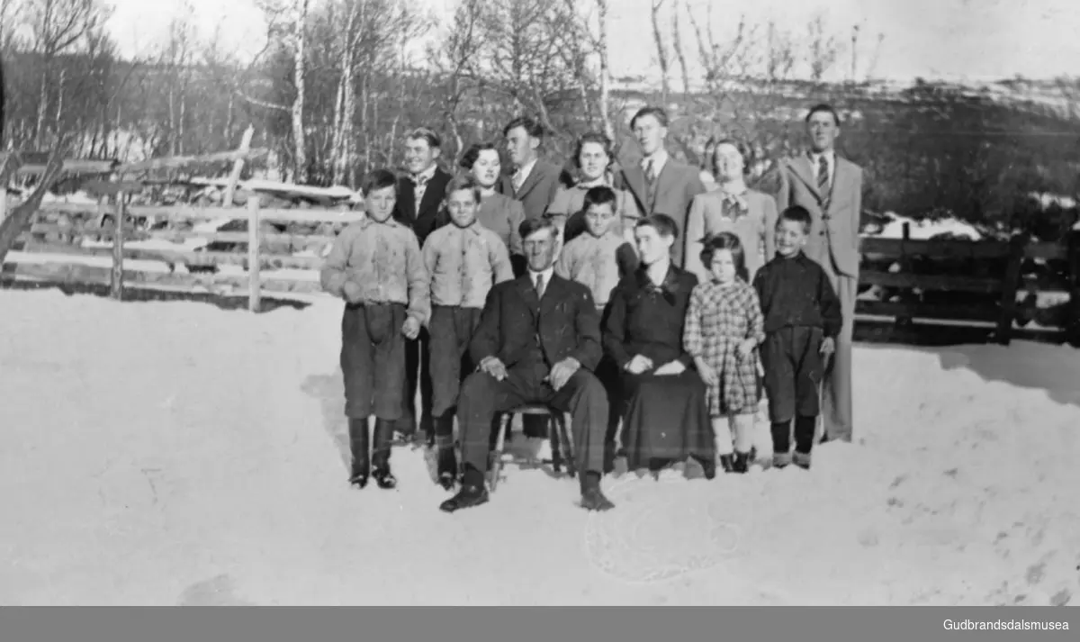 Familien til Karl og Marie Kveum samlet på gårdsplassen, totalt fjorten personer inkludert barn, det er vinter. 