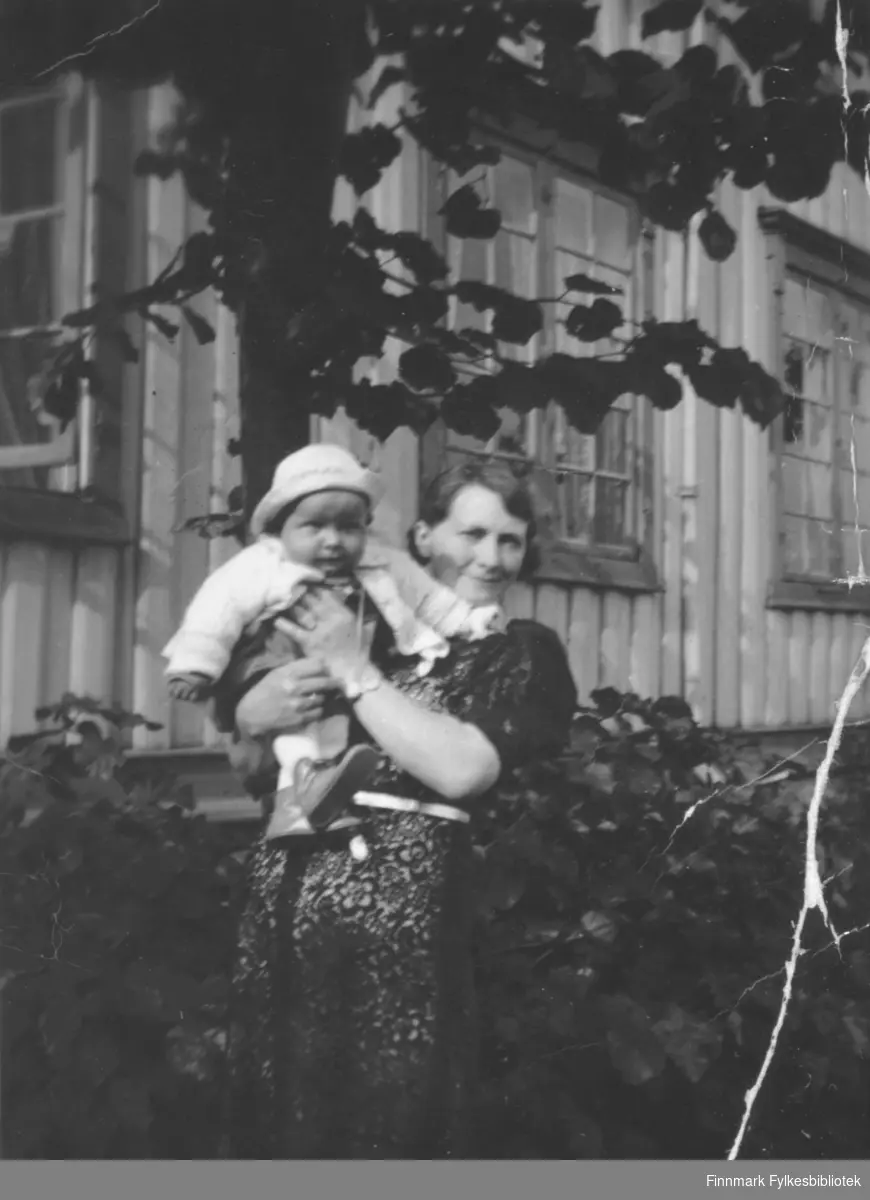 En kvinne holder et lite barn i armene. Sted og personer er ukjent, men det kan være Ragnfrid Elise Karlsen med sønnen Arne Martin.