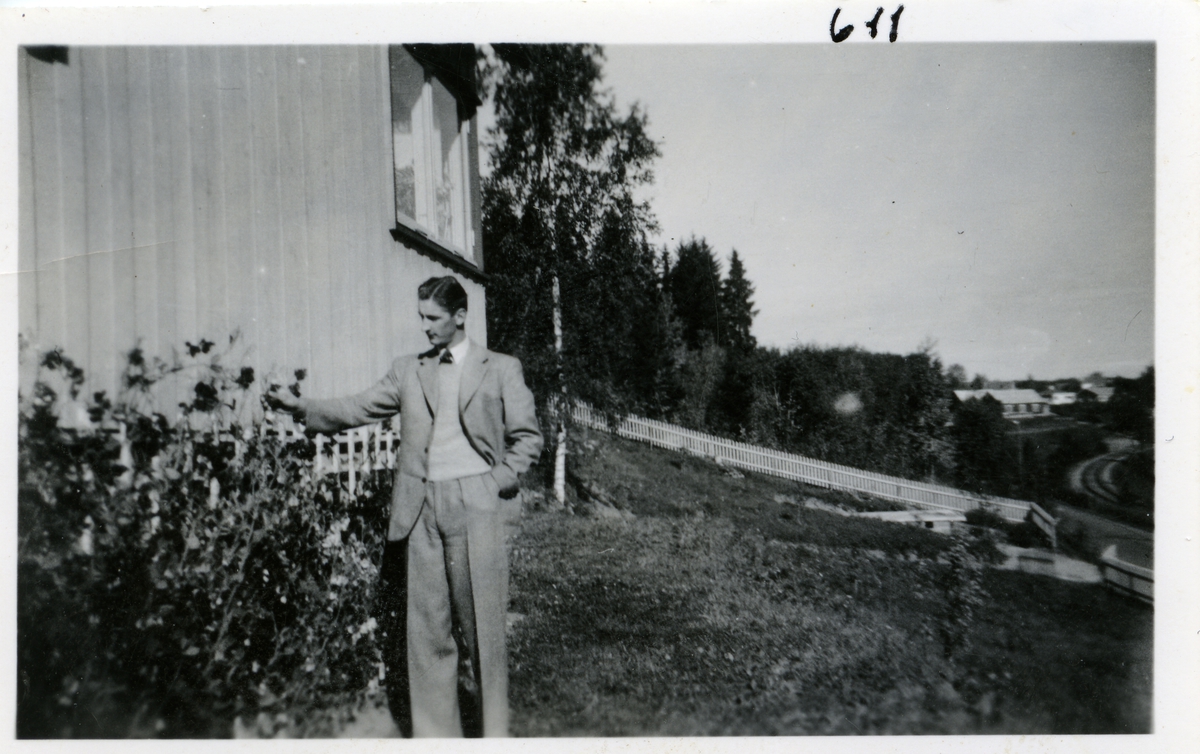 Bildet viser en ung mann som står ved en rosebusk utenfor et hus. Toralv Buskern fra Skreia
