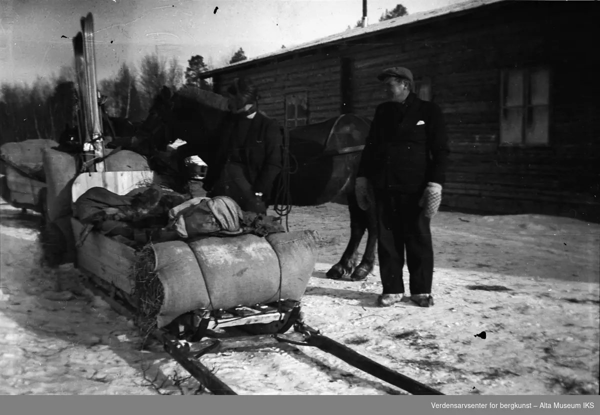 En mann og en kvinne står blant hester og sleder utenfor en fjellstue.