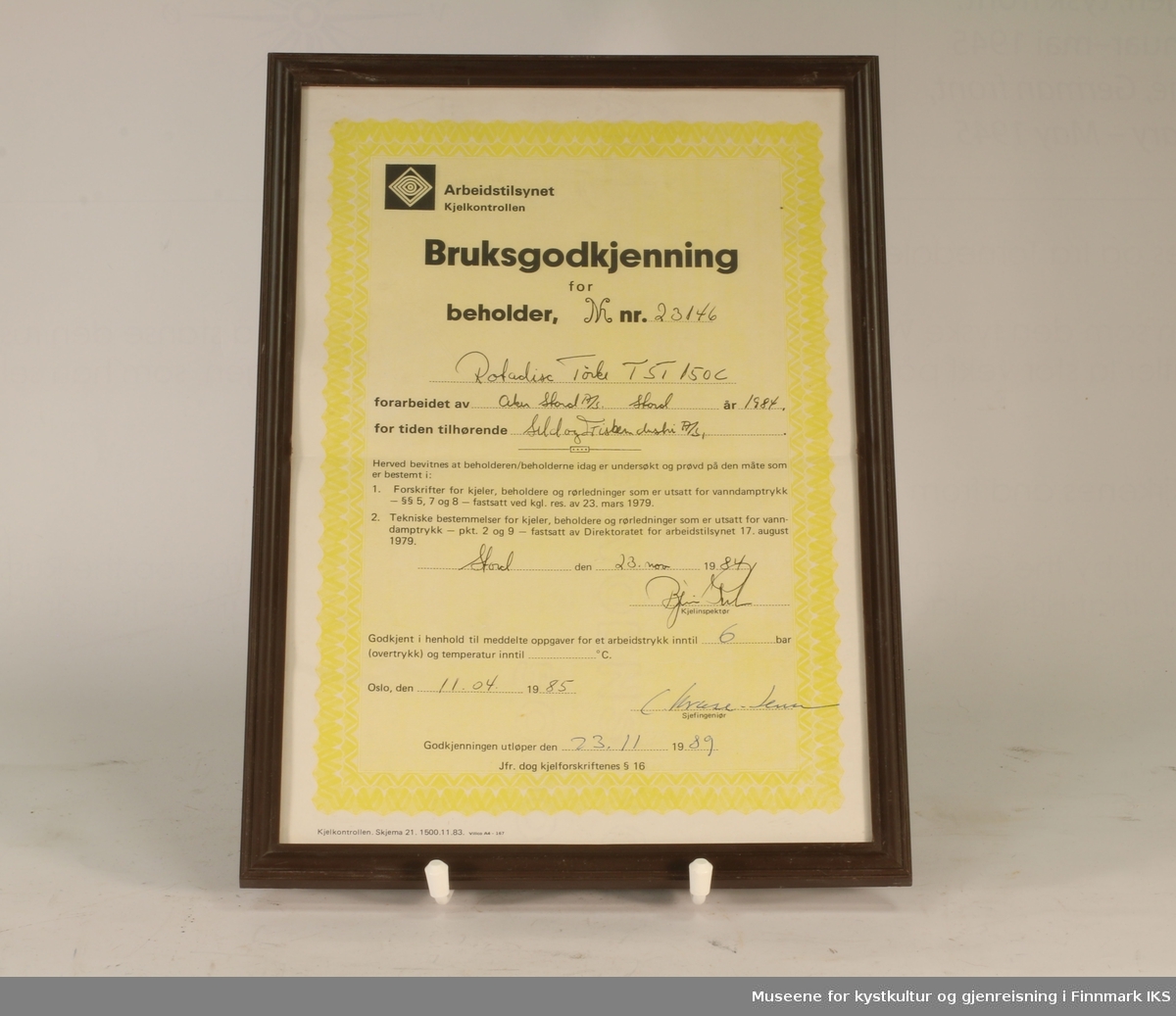 Bruksgodkjenning for Rotadisc Tørk TST 150C (beholder nr. 23146) hos Sild & Fiskeindustri AS, utsendt av Arbeidstilsynet Kjelkontrollen i 1985. Hvitt og gult papir med sort tekst. Utfylt for hånd. Innrammet.