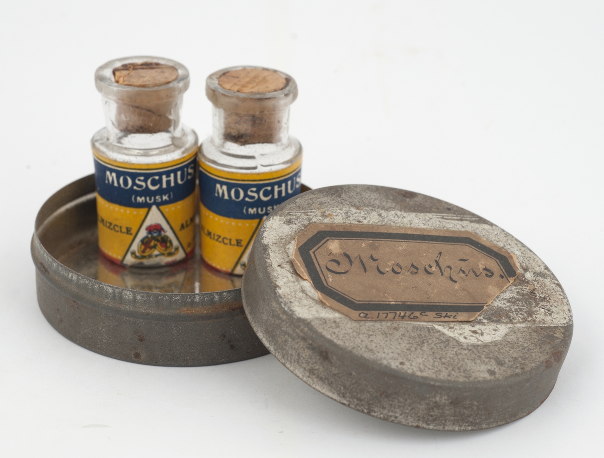 To små medisinglass med kork i rund metalleske merket Moschus.
Inneholder et brunt pulver.
Karakteristisk lukt