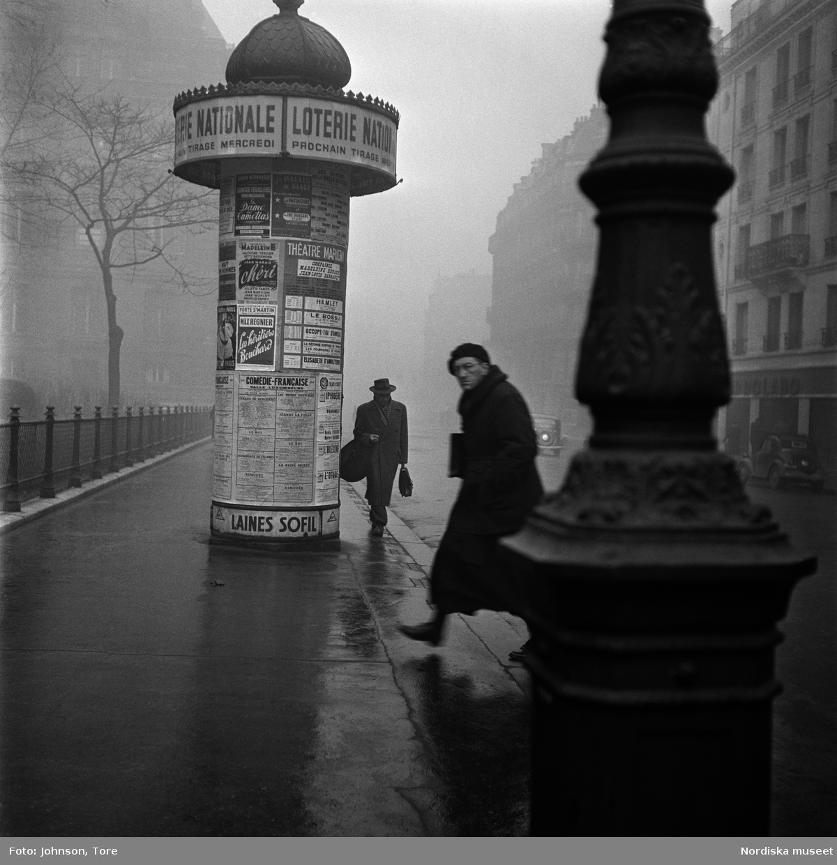 Fotgängare på en gata i Paris, annonspelare i bakgrunden.