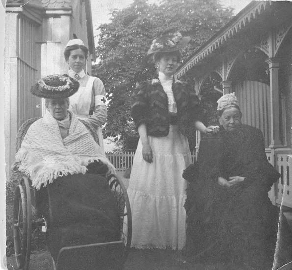 Text till bilden: "Mia Åhlström i rullstol, (troligen dotter Maria Fredrika) bakom henne, en sköterska, därefter Thora Åhlström i mitten samt doktorinnan Johanna Beata Sofia till höger".