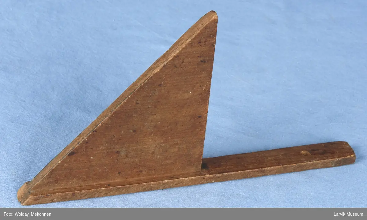 Form: En smal list er påmontert en trekant med to rette sider og en skrå. Hull øverst i listen.
