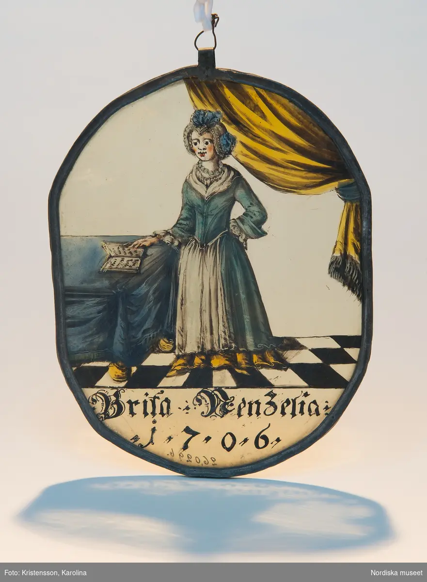 Fru Brita Nenzelius stående på ett rutat golv. Till vänster ett täckt bord med en bok, till höger ett draperi. Hon bär en blå klänning med vita isättningar, runt halsen ett halsband. Text: "Brita Nenzelia 1706".