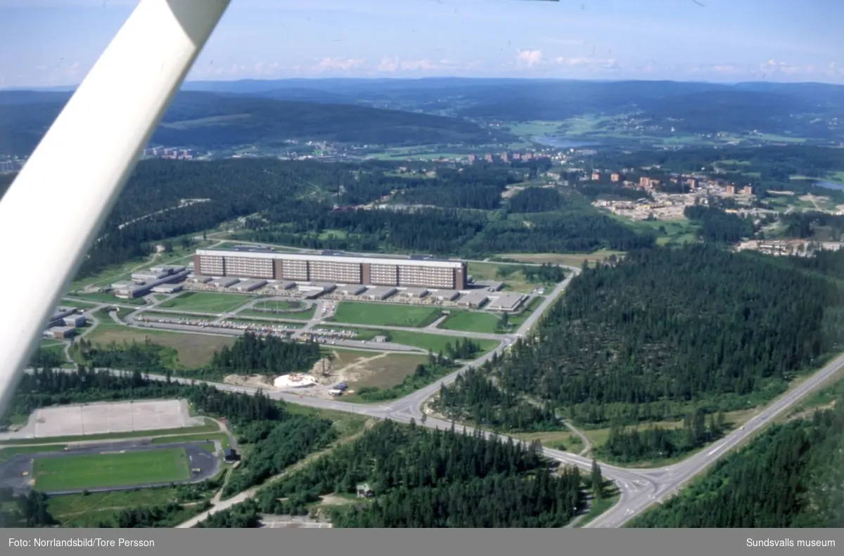 Flygfoto över Sundsvalls sjukhus taget västerut med Baldershovs idrottsplats i nederkant och det pågående bygget av bostadsområdet i Granloholm till höger.