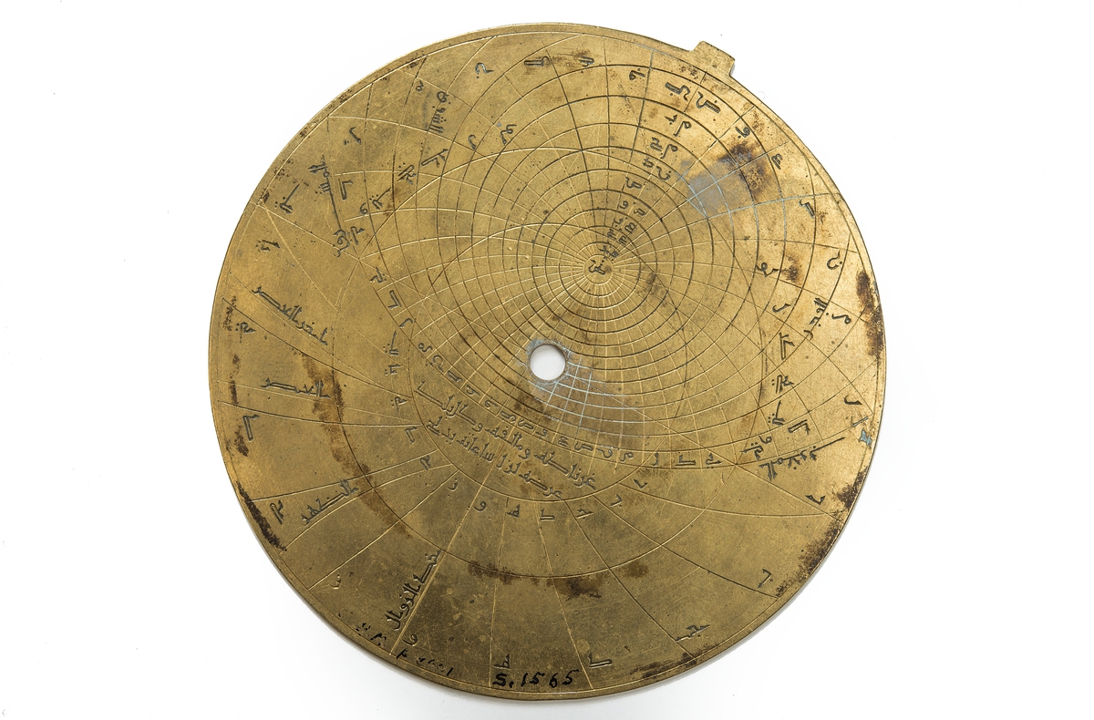 Made of brass n 729 A.H. (after Hedschan) =year 1328-29. 
It was bought it in Marocco in 1907 and was made by Ahmad ibn Ali Sarafi in Spain, Alcalá (nearby Sevilla).
The practical use of the astrolabe is to find the time during the day or night (by altitude of the sun or the stars) and the time of a celestial event such as sunrise or sunset and as a handy reference of celestial positions.
The astrolabe is made up of several separate parts. The main-part is a disc of brass called the Mother (Mater). Into the Mater fits seven thin discs, called the plates or tables. The seven plates are each engraved and represent the usual projection of the sphere varied only for the particular latitudes for which each was made.
