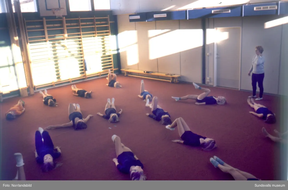 Gymnastiklektion på Nackstaskolan. Större delen av flickorna har tidstypisk klädsel i form av sockiplast och mörkblå gymnastikdräkt.