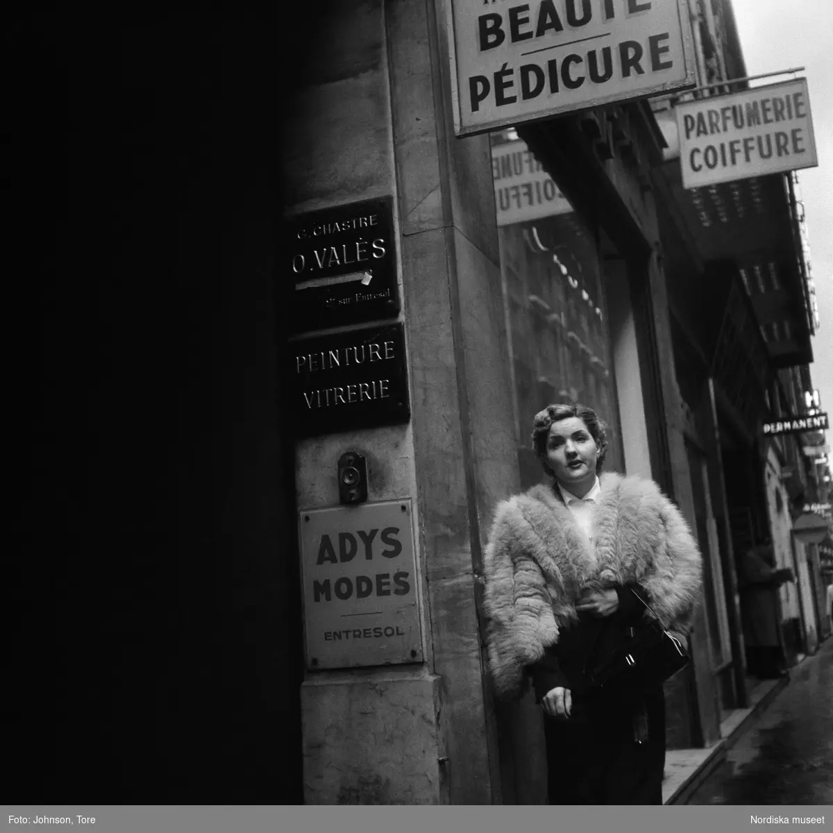 Paris. Kvinna i päls på gata utanför skönhetssalong.