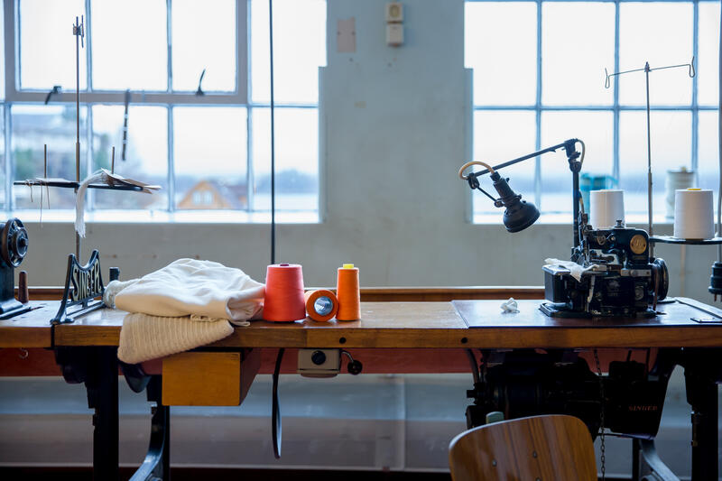 symaskin på trebord i fabrikklokale, oransje og raud sytråd