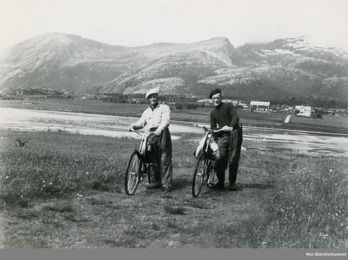 To menn med sykler på gården Nylandet i Saursfjord, ca. 1940- 50. Til høyre er Petter Willumsen med en laks hengende på sykkelstyret.
