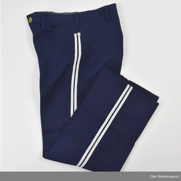 Marineblå bukse fra Lambertseter skoles musikkorps til barn. Buksen har to hvite striper langs siden av hvert bein. knapp og glidelås i metall.