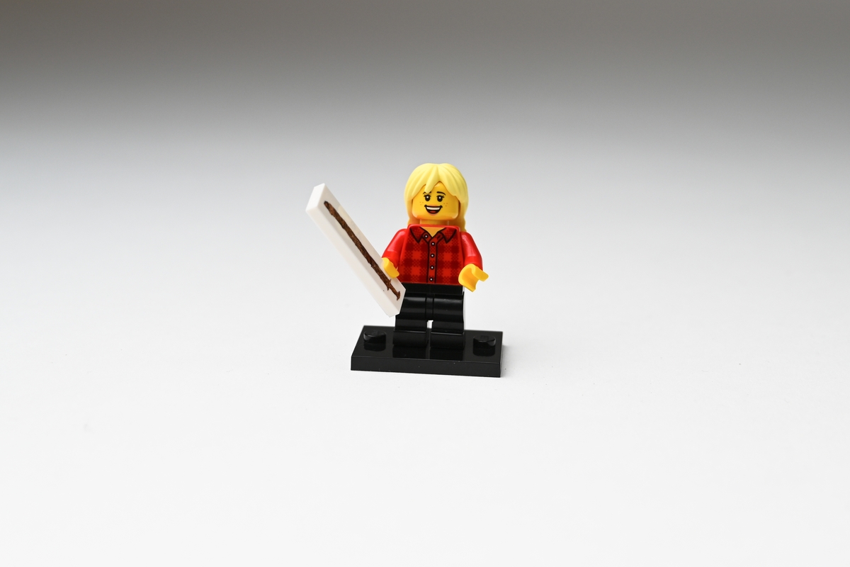 Legofigur av plast föreställande en flicka som håller upp ett svärd i ena handen. Flickan har gult hår i två flätor på ryggen, är klädd i röd- och svartrutig skjorta och svarta byxor. Figuren står på en svart platta. På en vit avlång platta, som figuren håller i handen, finns en bild av svärdsfyndet från Tånnö socken, Jönköpings län. Se vidare Historik.

Figuren förvärvades i en liten plastpåse med fasthäftad pappersetikett.