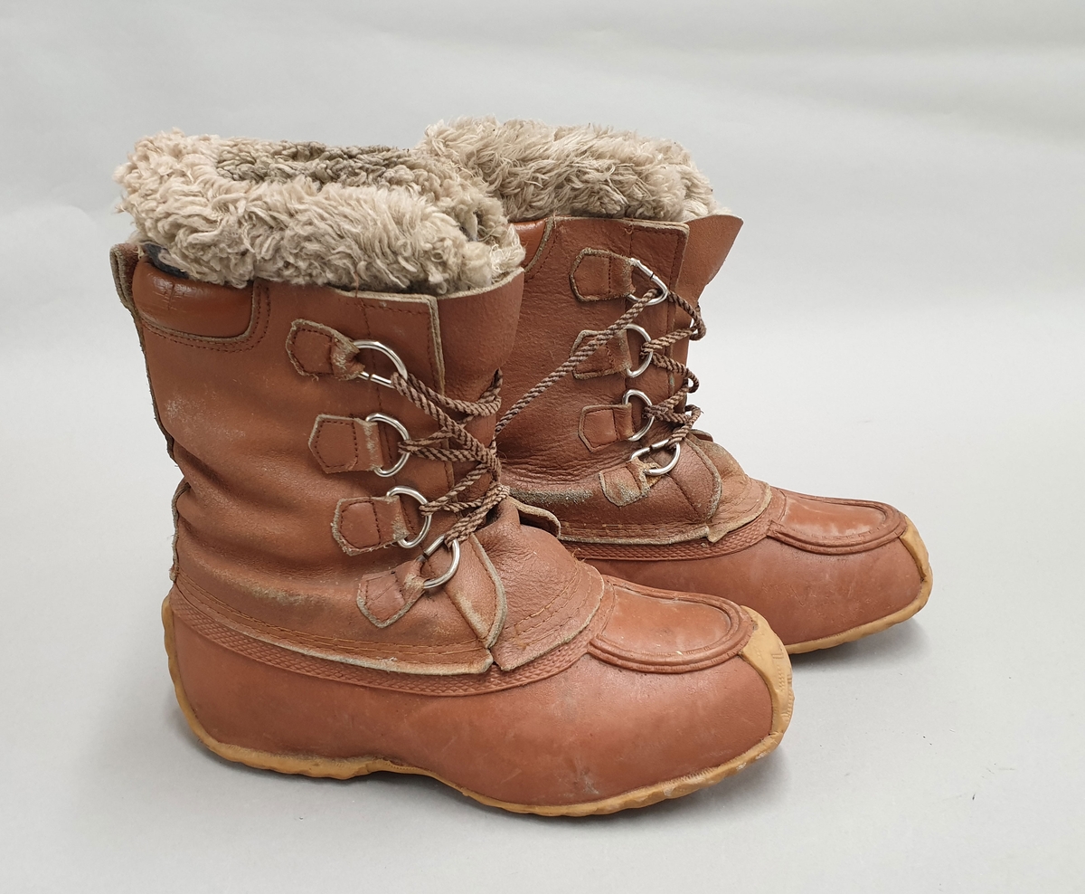 Vinterstøvler med uttagbart fôr av ullfilt. Sålen og skoen er av gummi, mens leggen er av skinn. Åtte beslag av skinn med metallbøyle som feste for lisser.
