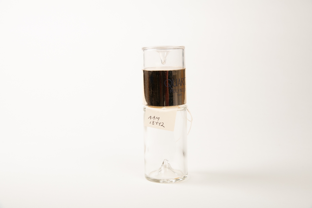Sylindrisk flaske av tykt glass, med en oppstående dråpeform i bunnen og innv. i lokket.  Lokket er øvre del av sylinderen og har tekst:   EAU DE PARFUM 850 og QUARTZ MOLYNEUX Paris