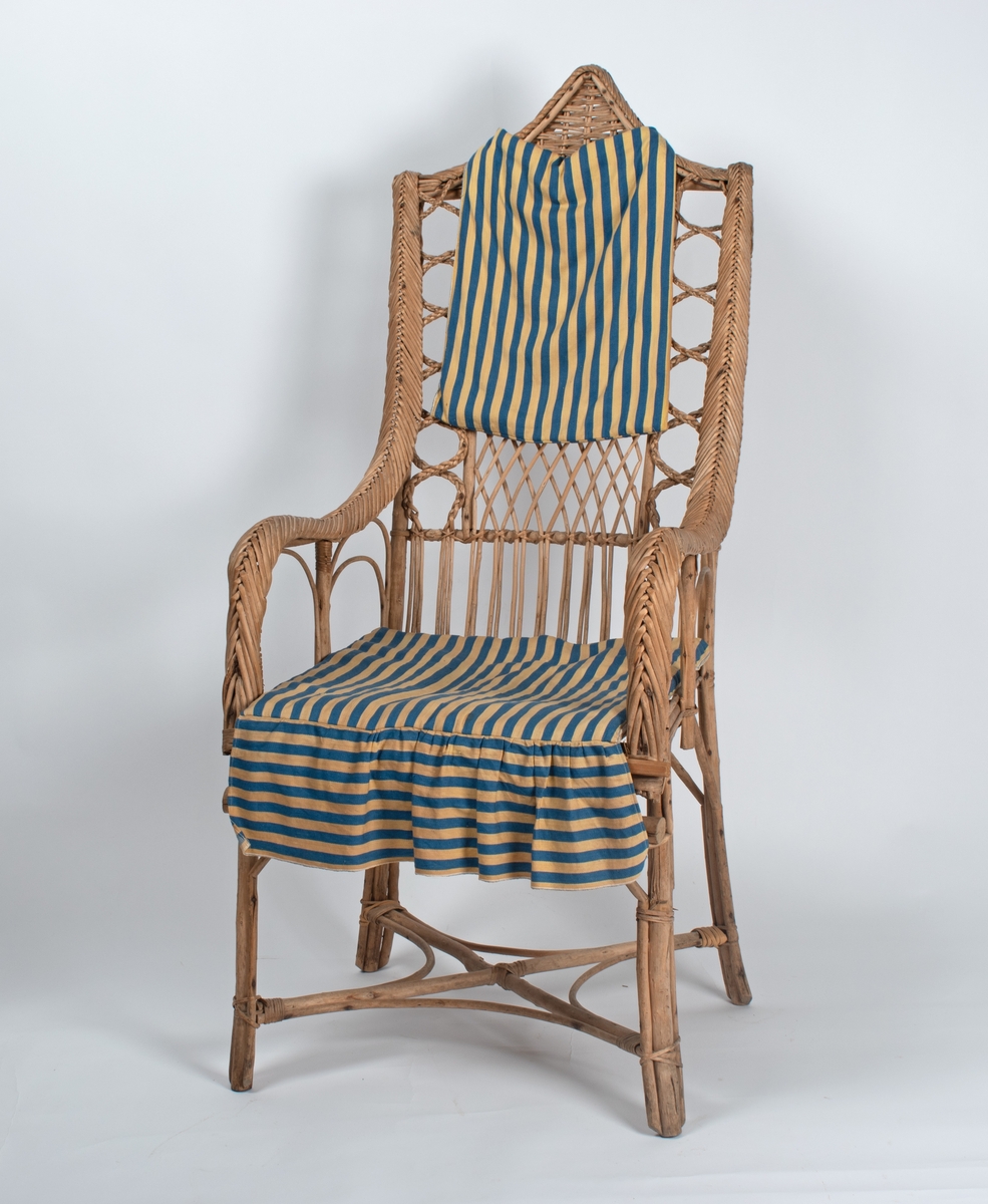 Kurvstol med høy rygg og armlener. Stolen har lett og åpen konstruksjon. Dekorative elementer med ulike typer fletting. Stolen har løs setepute og en liten, løs ryggpute.
