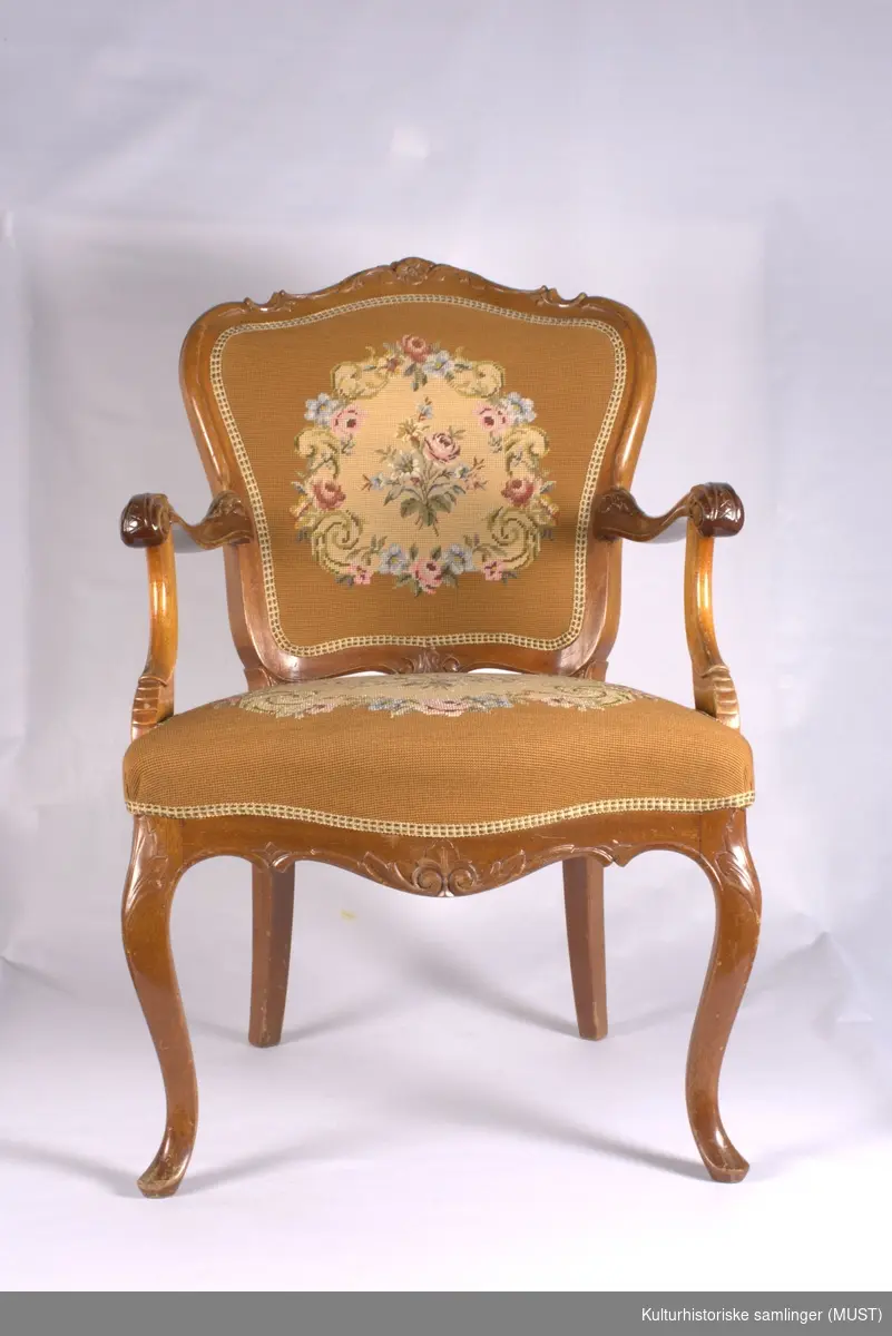 Armstol av mahogny med brodert trekk på sete og rygg. Svugne armelen, og frambein. Utskåret med blomster og akantus.