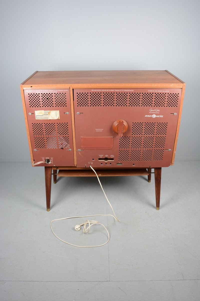 TV/fjernsyn samt radio monterte i kabinett med skyvedører for skjuling av fjernsynet når det ikkje var i bruk. Beteningsknappar og elektrisk kabel. Kabinettet har liggande rektangulær form.