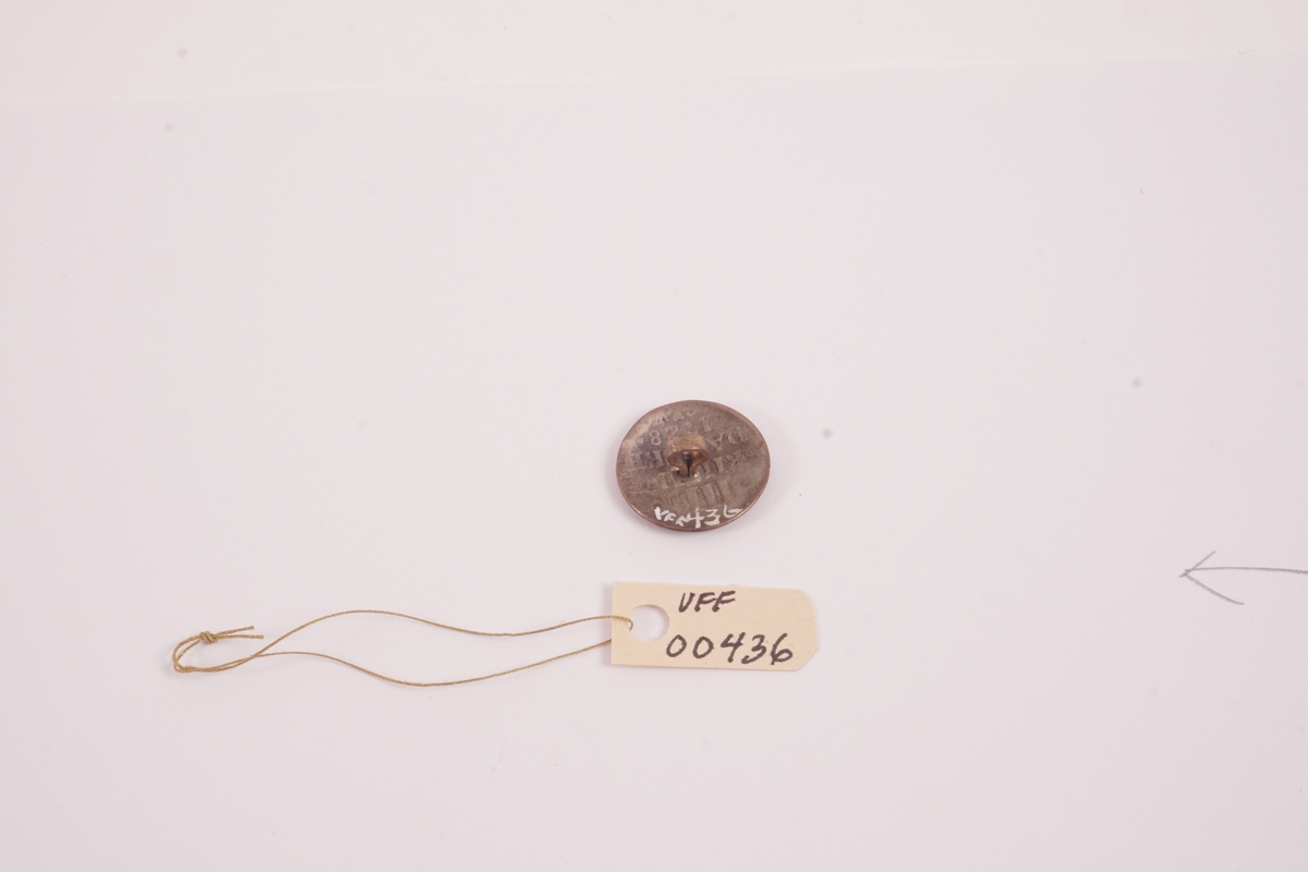 Knapp, støypt i forsølva kopar (?). Dansk mynt (skilling) 1728. Hempe av messing lodda på.