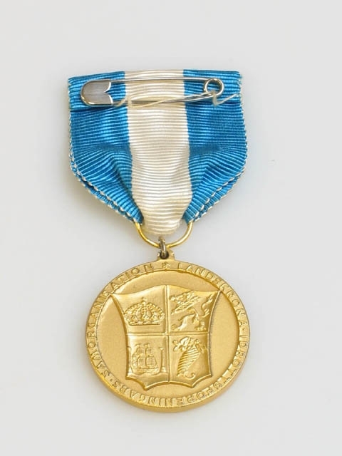Medalj med texten :"LANDSKRONA IDROTTSFÖRENINGARS SAMORGANISATION" som omringar Landskronas stadsvapen på ena sidan och texten: "FÖR BÄSTA IDROTTSPRESTATION 1961 LANDSKRONA G.I.F." på andra sidan. Stämplar : "RW", (oläsbar), "S", kattfot, "M9". M9 betyder 1960. Hänger i blått och vitt band, fästes på kläder med säkerhetsnål.
