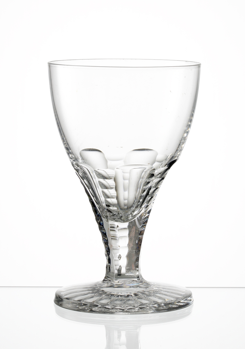 Design: Edward Hald, Orrefors. 
Ölglas. Kupa med lågt ben. Facett- och olivslipad nedre del av kupan samt ben. 
Fot med olivslipad botten.