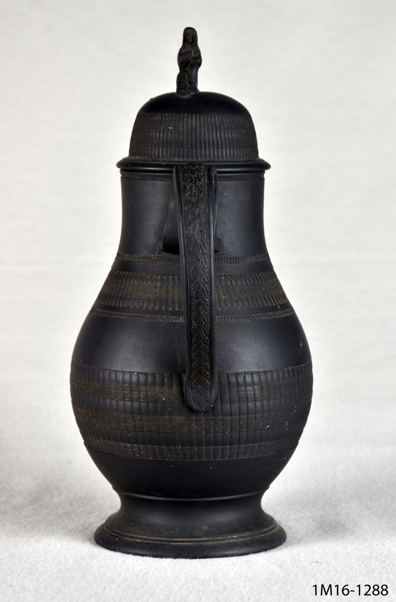 Kaffekanna, svart, basaltware. Lockets knopp utgörs av en kvinna i slöja, en form som ibland kallas änke-form.