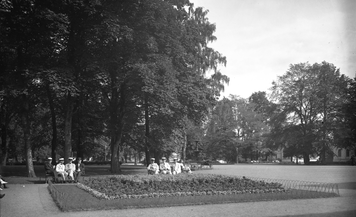 På bänkarna i Rådhusparken i Jönköping sitter några ynglingar med studentmössor. I bakgrunden skymtar Riksbankens hus.