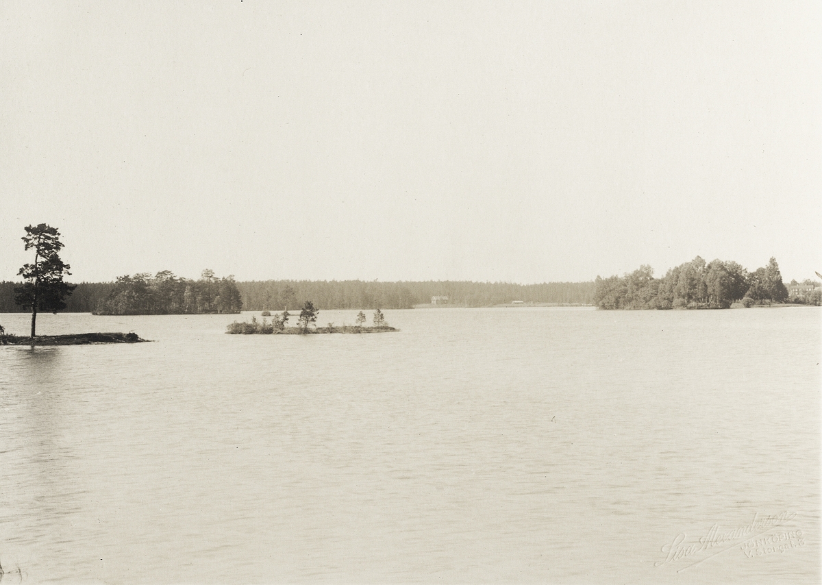 Orrefors glasbruk. Foto av en sjö med några mindre holmar. Till höger ...