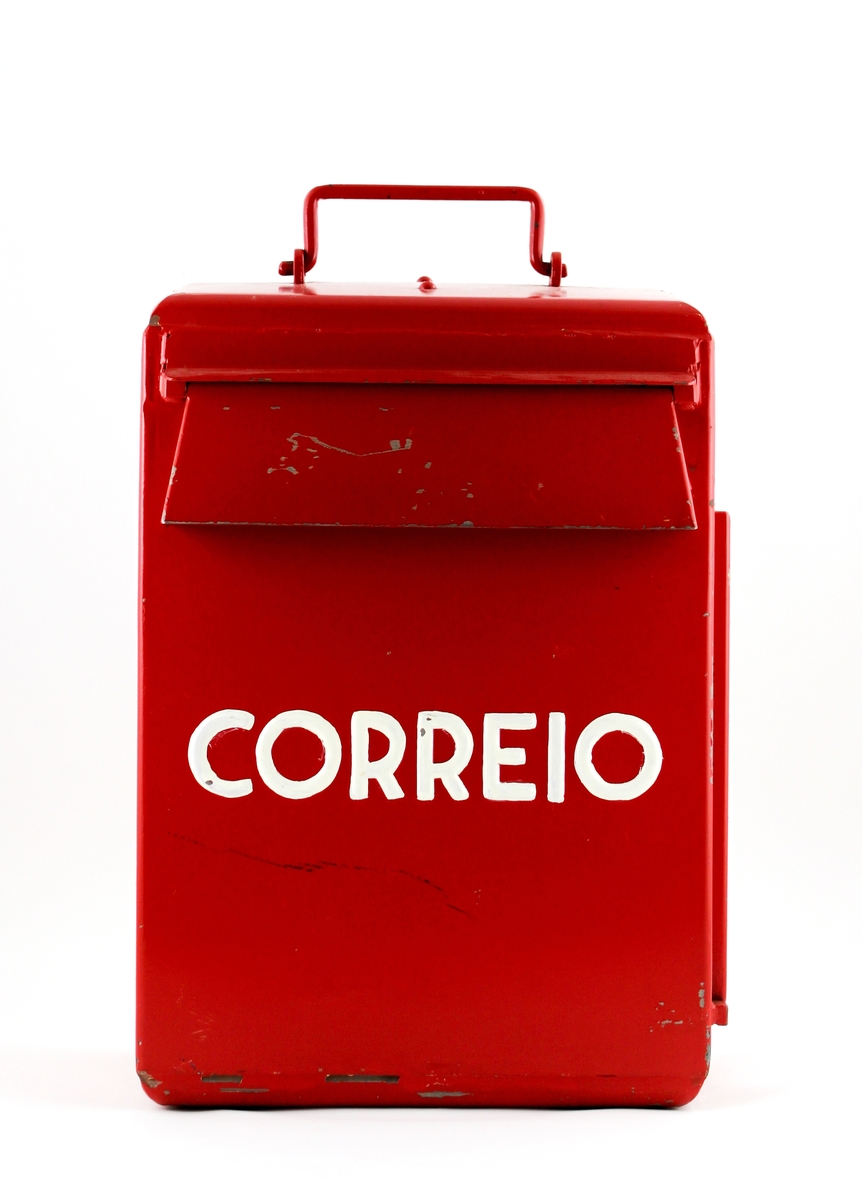 Brevlåda i rödmålad järnplåt från Portugal. Med lockförsett brevinkast på fronten. Ovantill är ett handtag placerat. Brevlådan tömmes genom en lucka på höger kortsida. Två nycklar finns.
Fastsättningsanordning och skruvar förvaras i brevlådan.