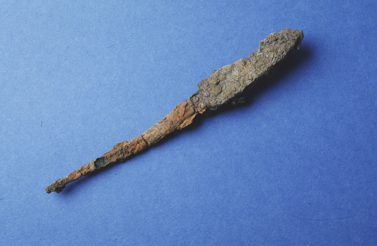 Ein kniv av jern i fem delar med restar etter treskaft. Bitane er limt saman. Både blad og tange er bevart. Bladet l. 60 mm, b. 19 mm og 5 mm t. Tangen l. 91 mm. St. l. totalt 155 mm. (Fnr 198).
