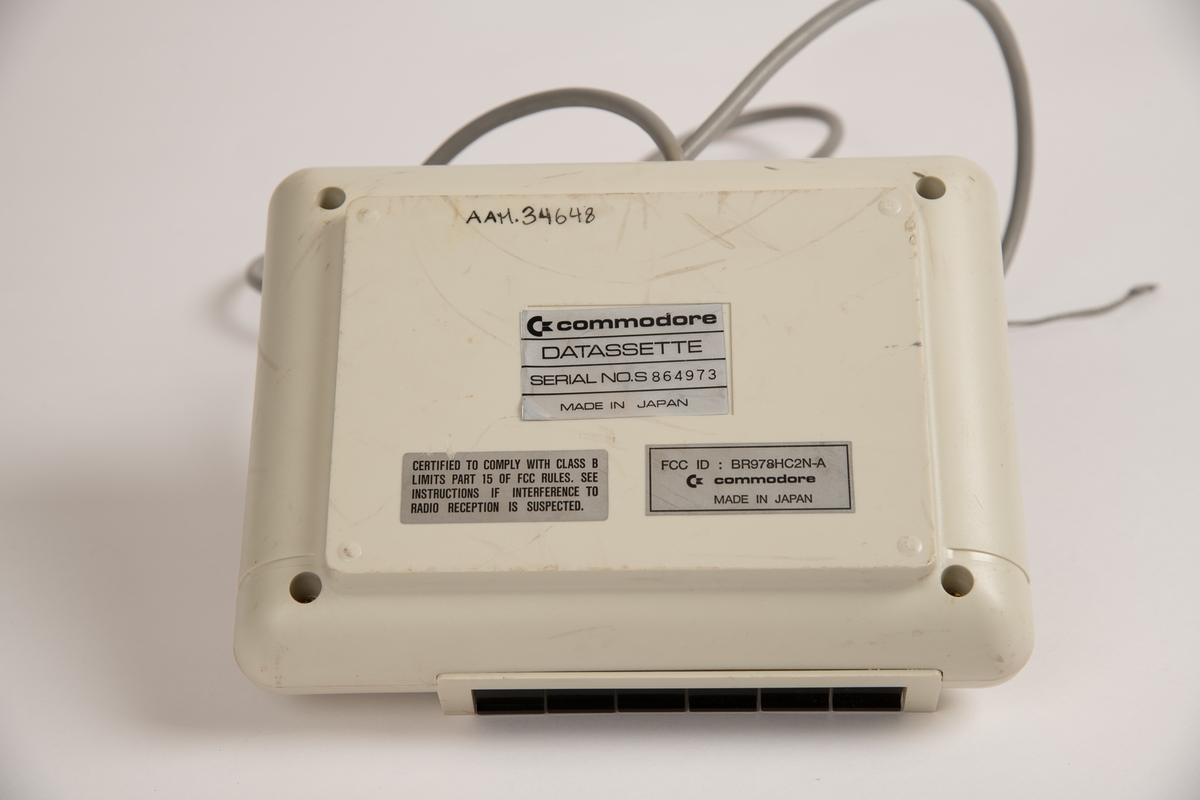 "Kassettspiller" til Commodore 64. Tilkoblet er en grå ledning som skal kobles i Commodore 64 tastaturet. 
Kanpper til "record", "play", "rewind", "fast forward (f. fwd)", "stop" og "eject".