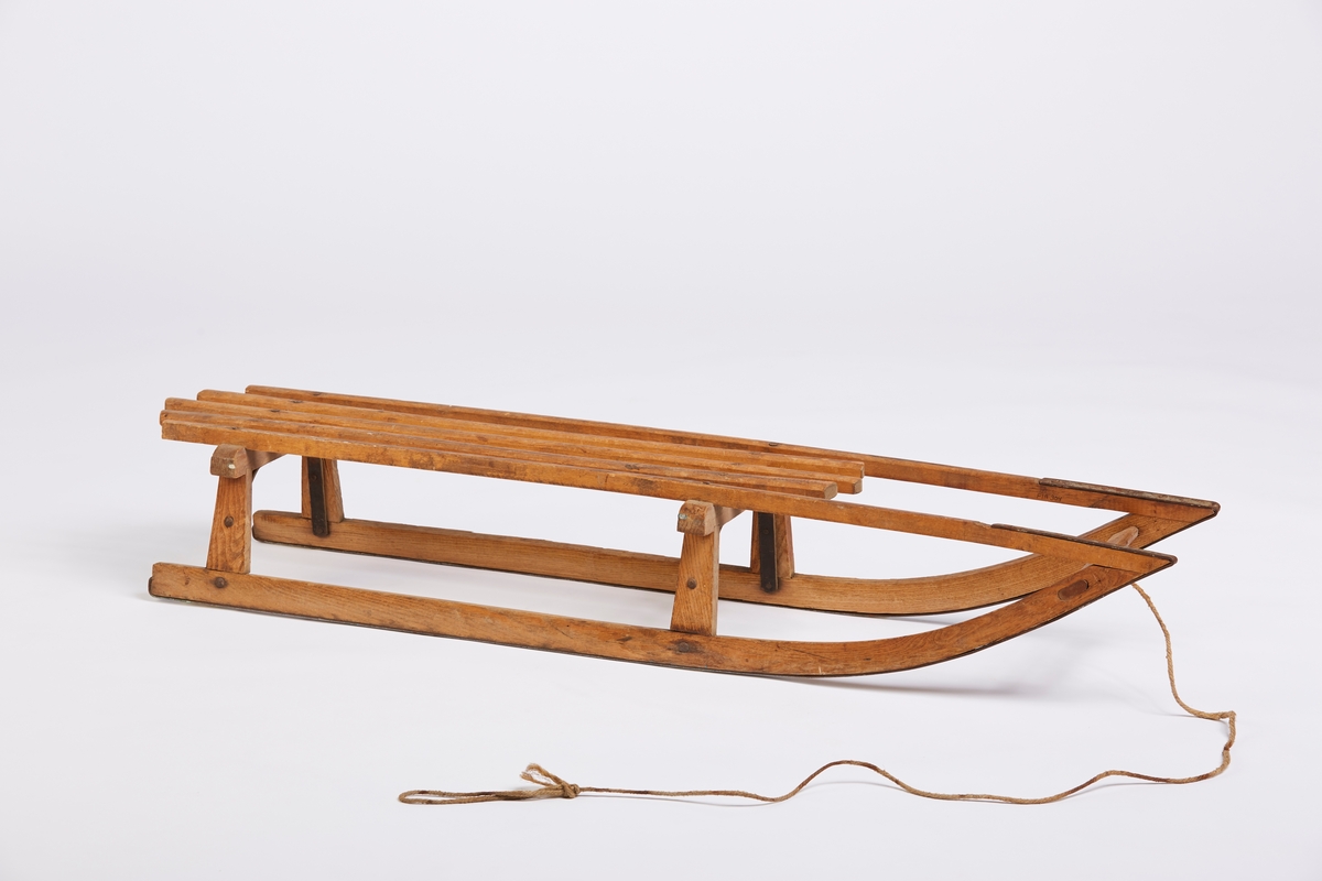 En tradisjonell trekjelke med påskrudde stålbånd under meiene. 5 spiler i setet. Kjelken har trekksnor med løkke.