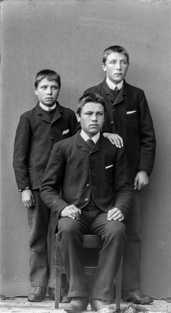 Tre yngre menn, antatt brødre med mørkblondt hår, kledd i mørke dresser og kvite sjorter med slips.