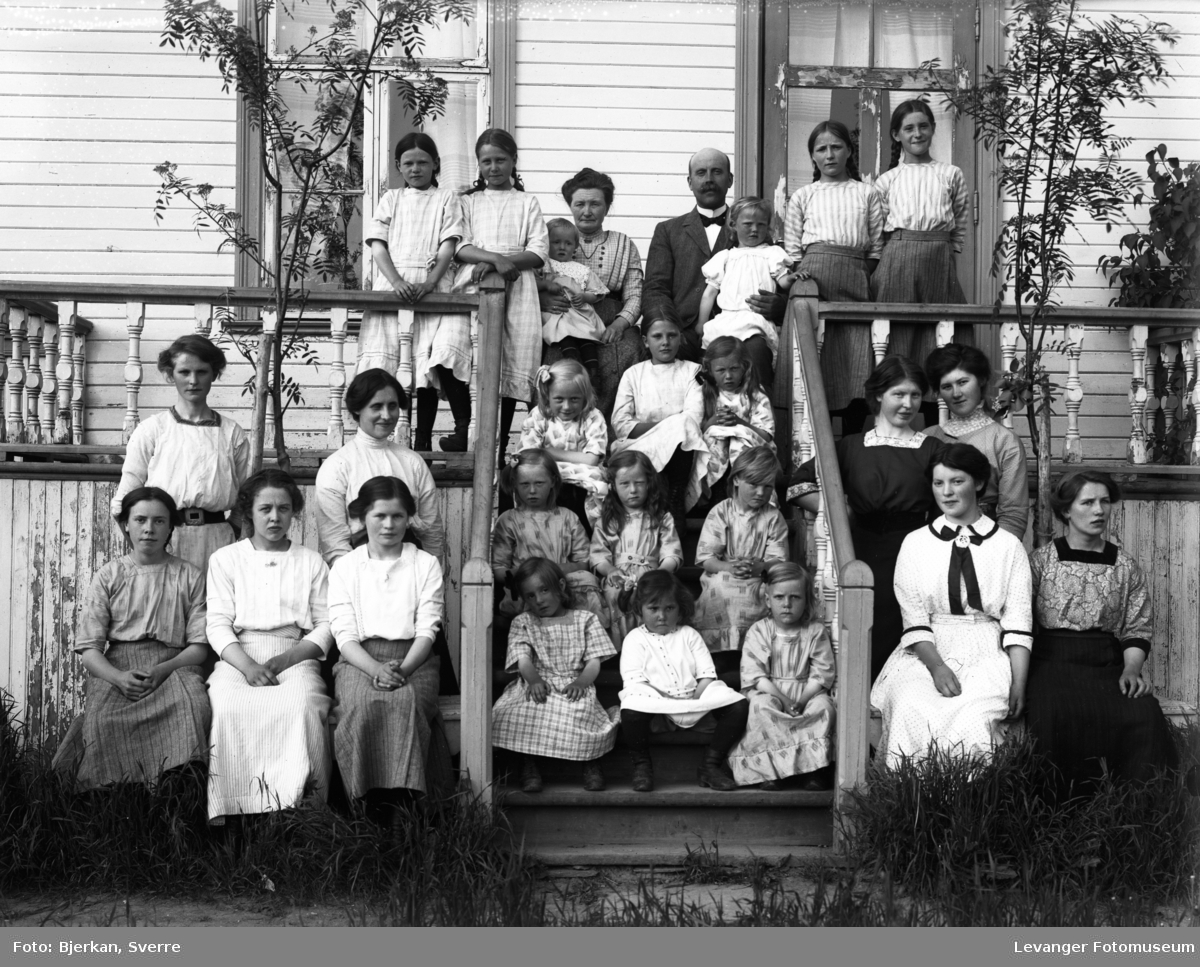 Gruppebilde av mann, kvinner og barn stående i trapp foran bygning. Barnehjem