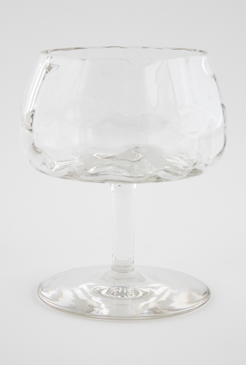 Rødvinsglass i klart glass. Begerformet kupa som er dekorert med punktdekor. Hviler på en enkel stett og en flat sirkulær fotplate.