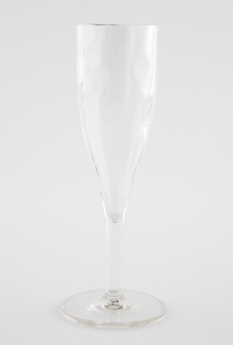 Champangeglass i klart glass. Konisk kupa som er dekorert med punktdekor. Hviler på en enkel stett og en flat sirkulær fotplate.