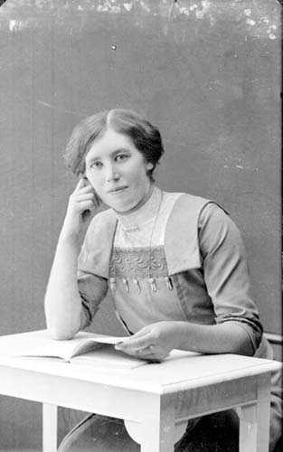 Porträtt av en ung kvinna som sitter vid ett litet bod med uppslagen bok framför sig.